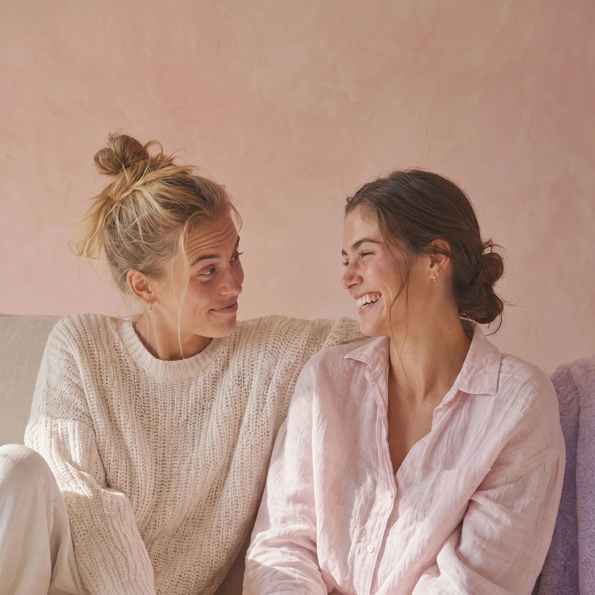 Two women mid-conversation, one smiling with a raised eyebrow, the other laughing.