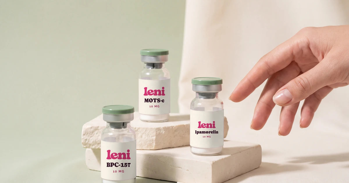 Three Leni vials on a pale sage surface with a hand reaching in.