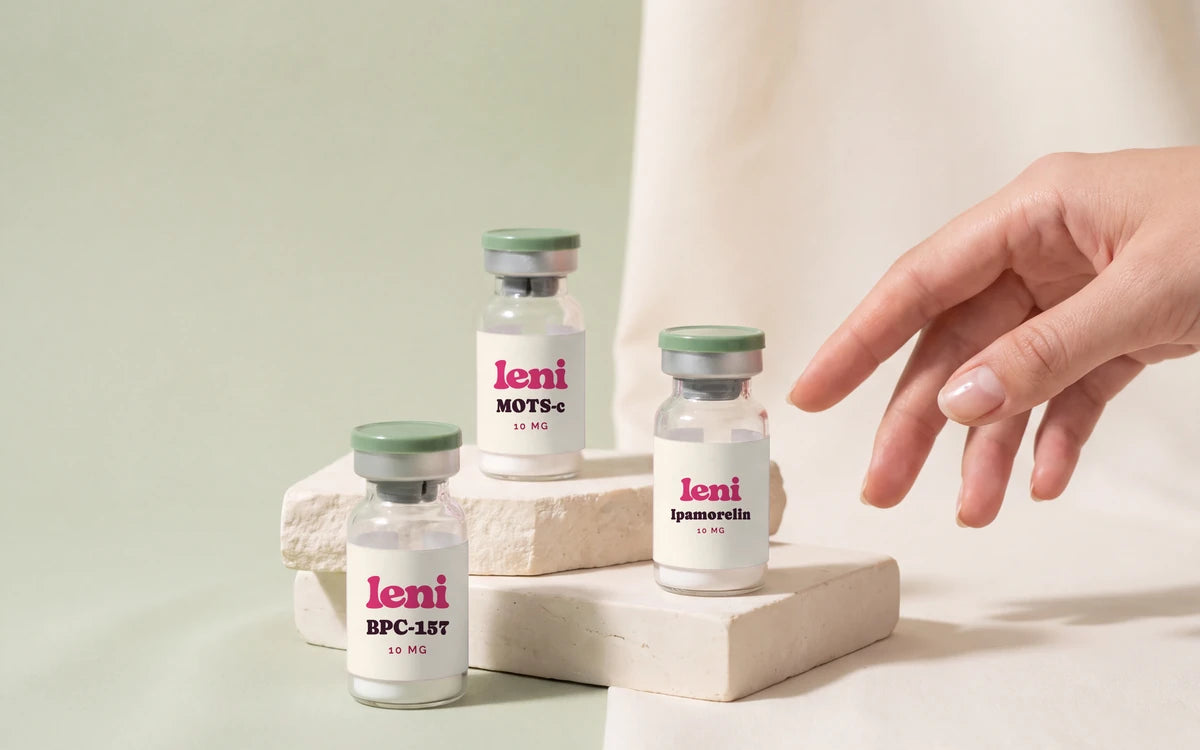Three Leni vials on a pale sage surface with a hand reaching in.